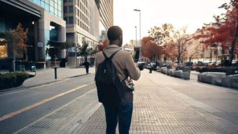 Pedestrian walks into frame on a busy street and pulls out a cellphone.